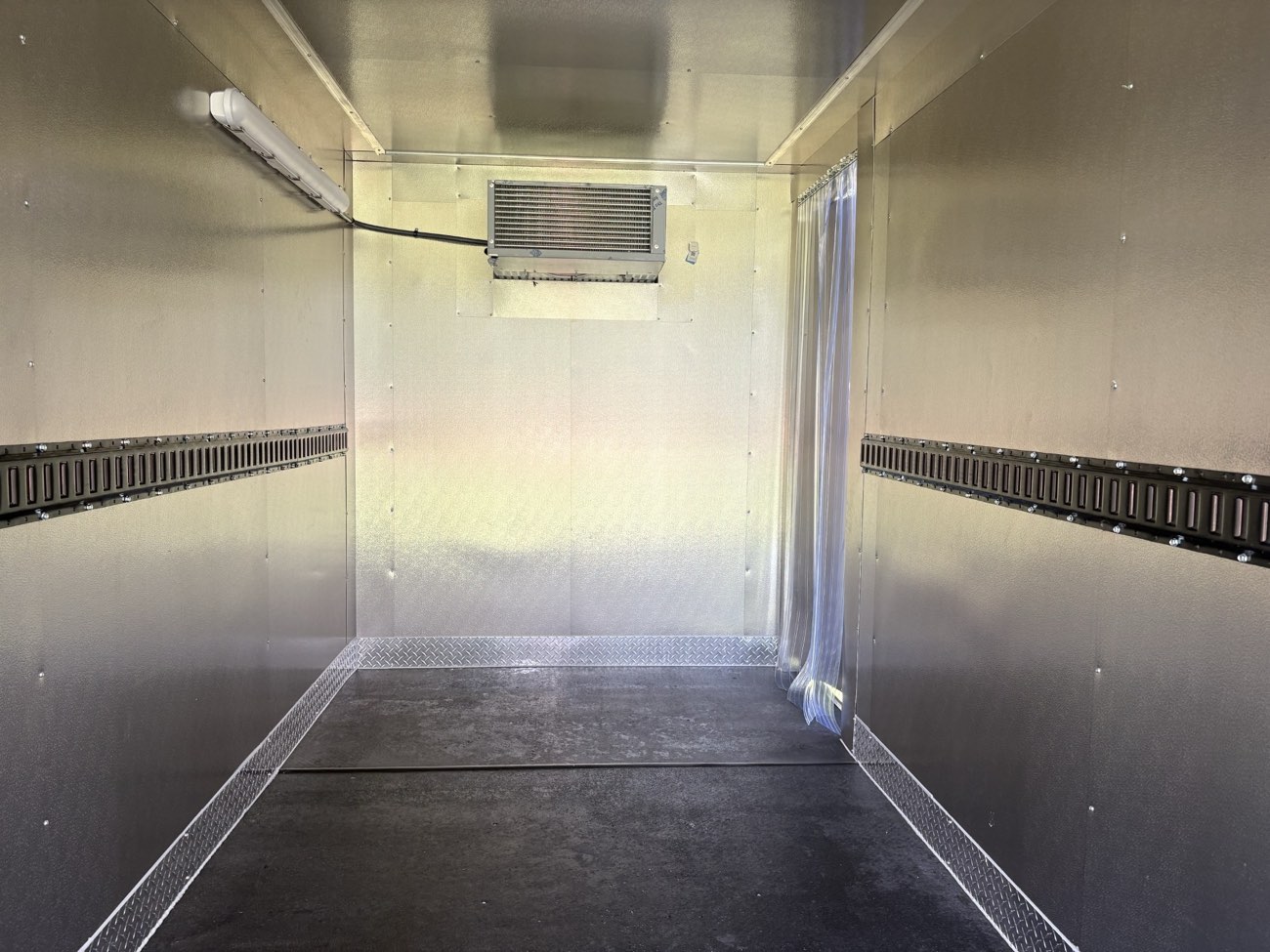 Interior of a Keep It Cool refrigerated trailer showing the ceiling-mounted refrigeration unit, interior light, wall tracks, and strip curtain